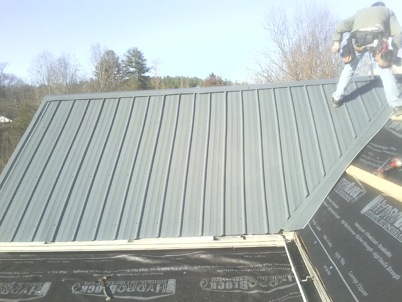 Crew installing dark green standing seam panels over synthetic underlayment in Startex