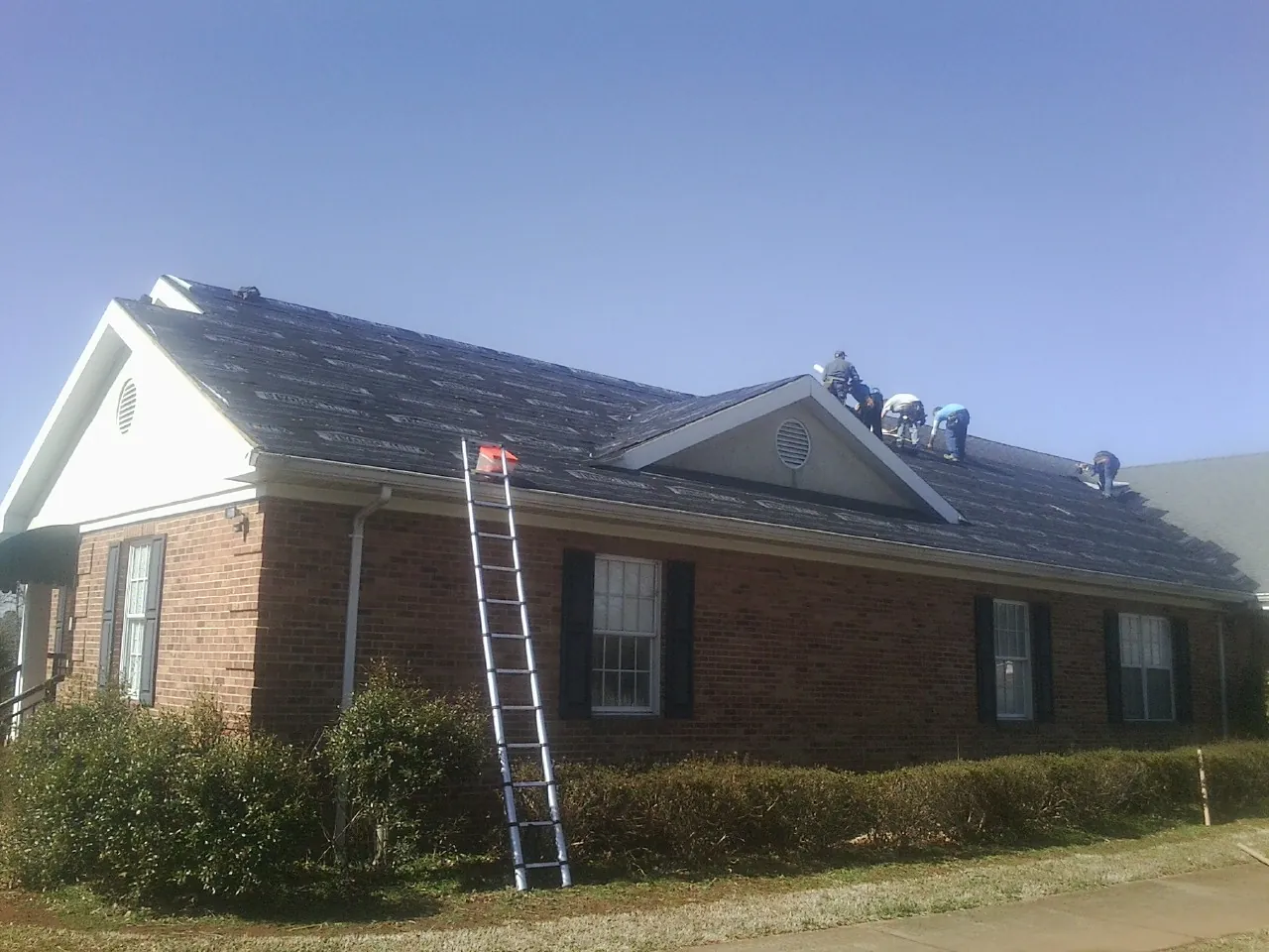 Crew tearing shingles off a brick ranch roof with a ladder set — Metal Roof Repair work by our crew in Startex
