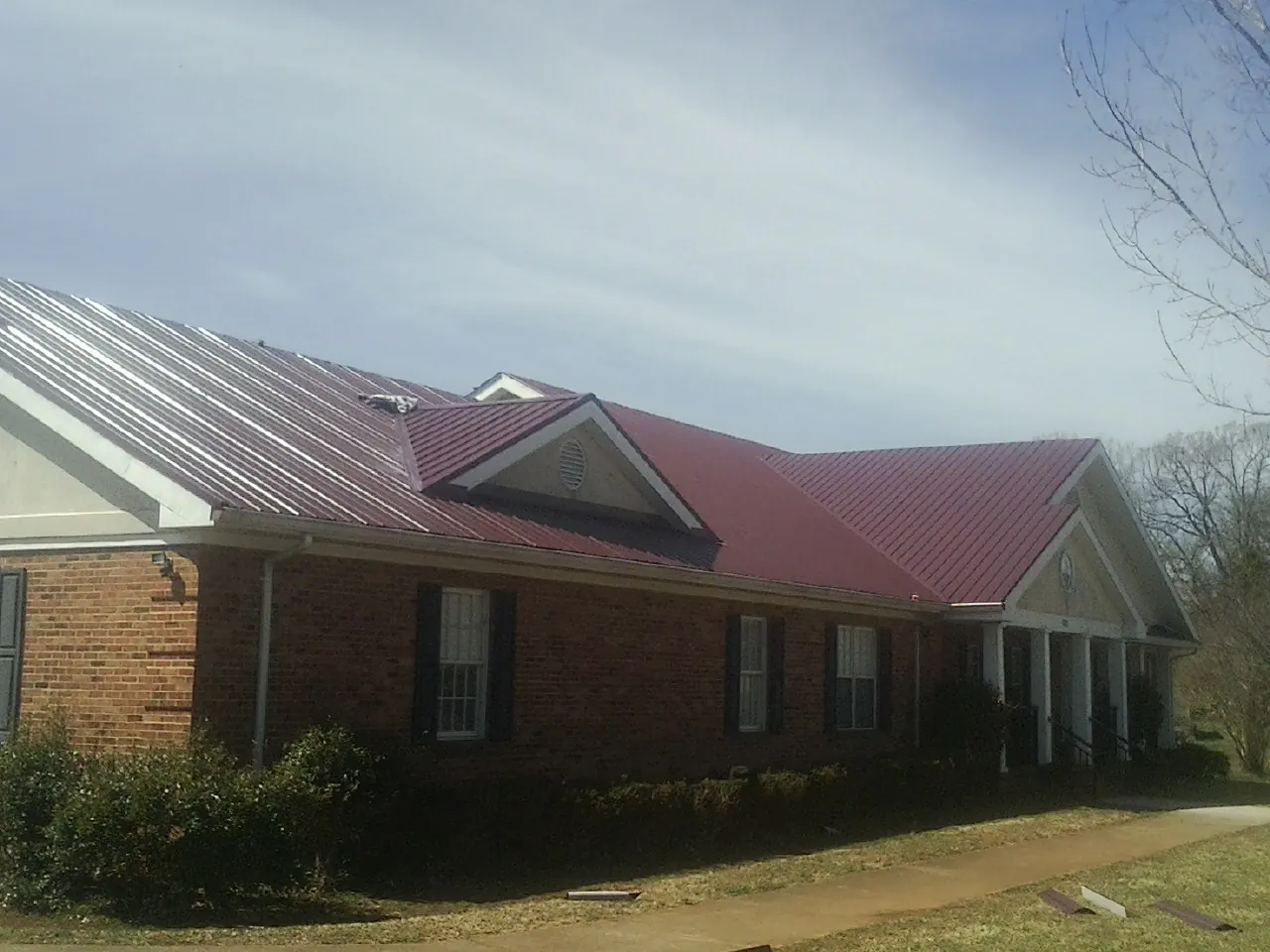 Red metal roof with gabled entries on a long brick building, from a Hail Damage Roof Repair job in Startex