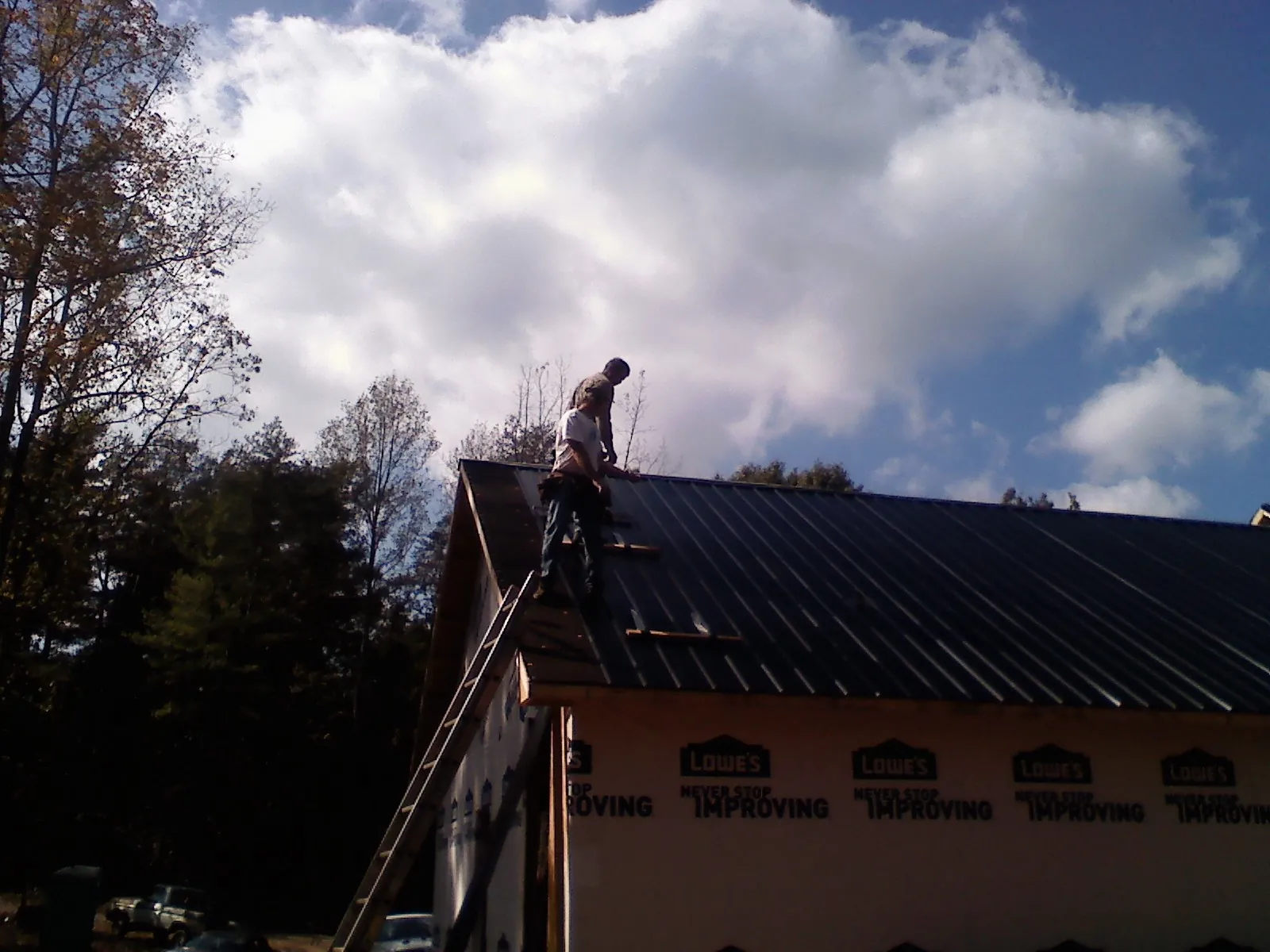 Roofer fastening dark metal panels high against a cloudy sky, from a Roof Inspection job in Startex